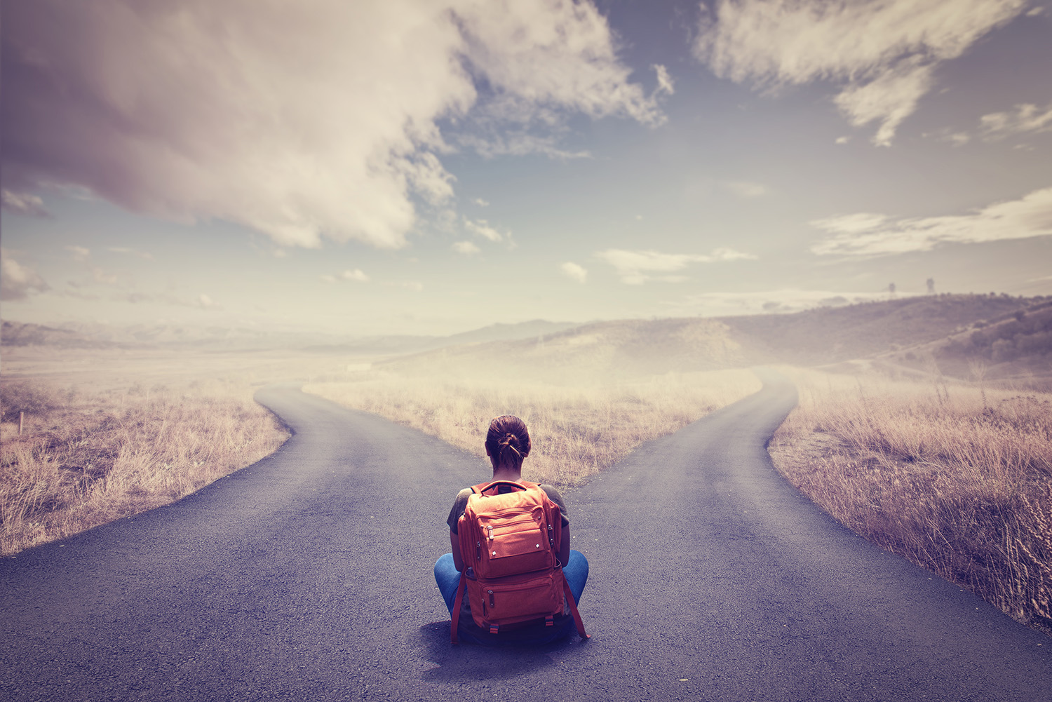 A person with a backpack sits at a forked road, contemplating which path to take.