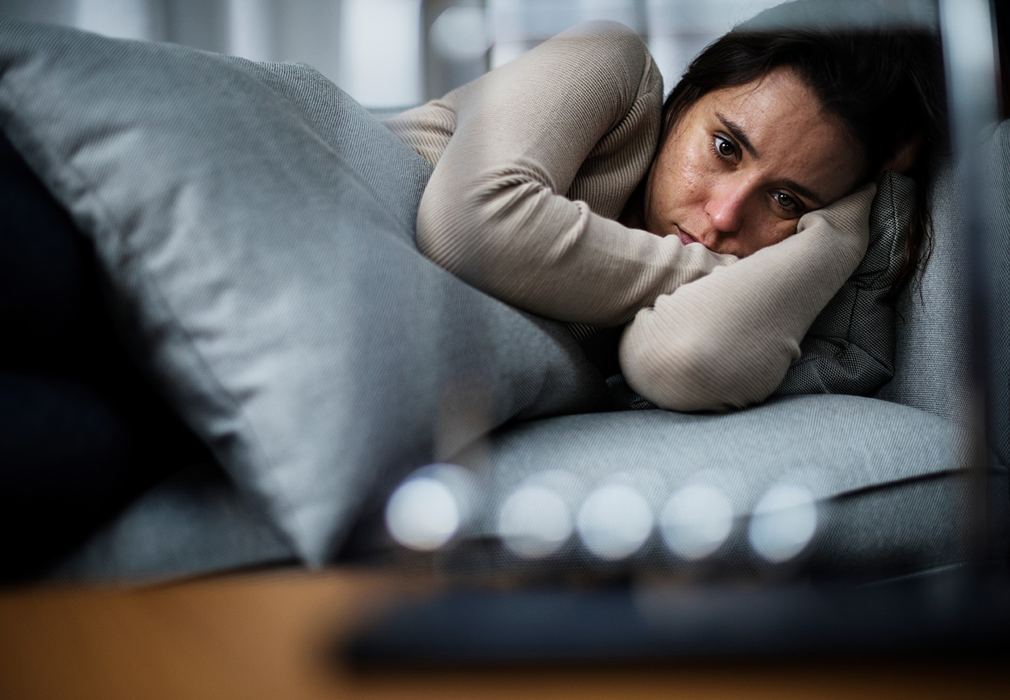 A woman appears distressed, lying on a couch with her face in her hands.