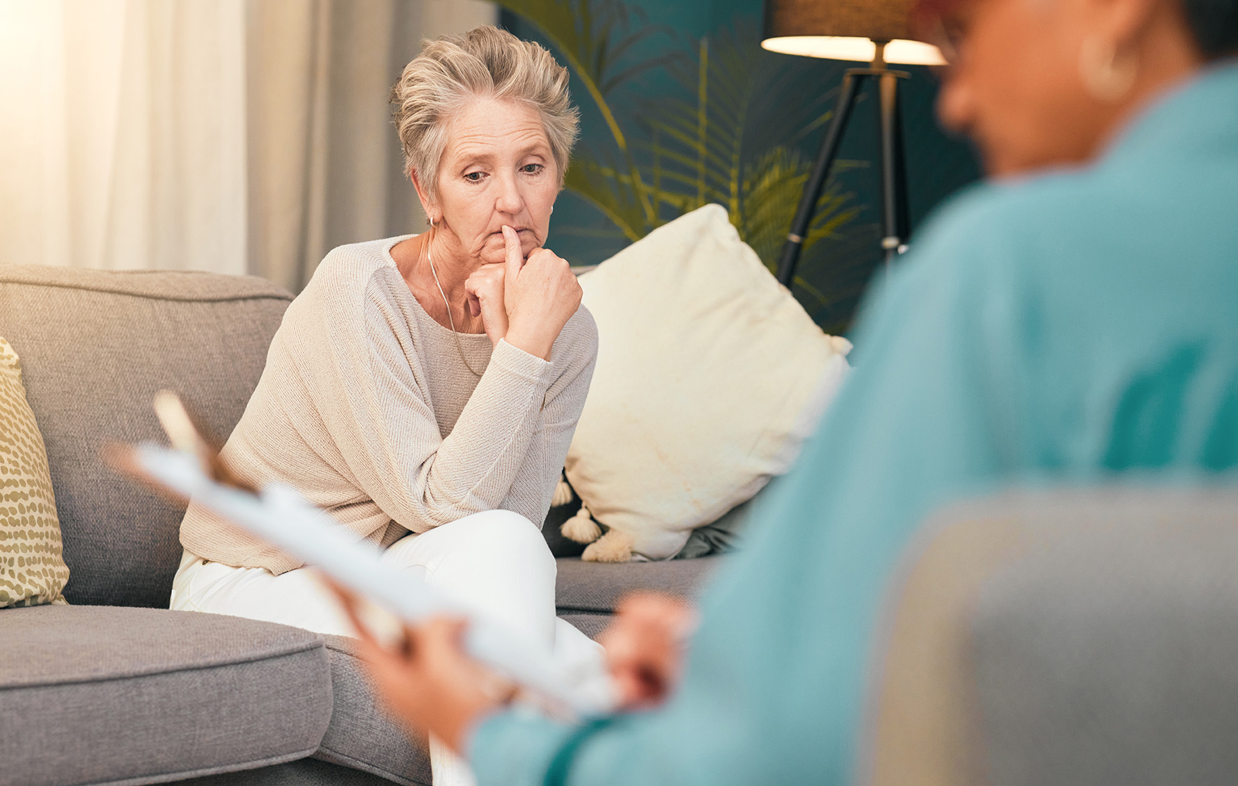 An older woman looks pensive during a discussion with possible therapist holding papers.